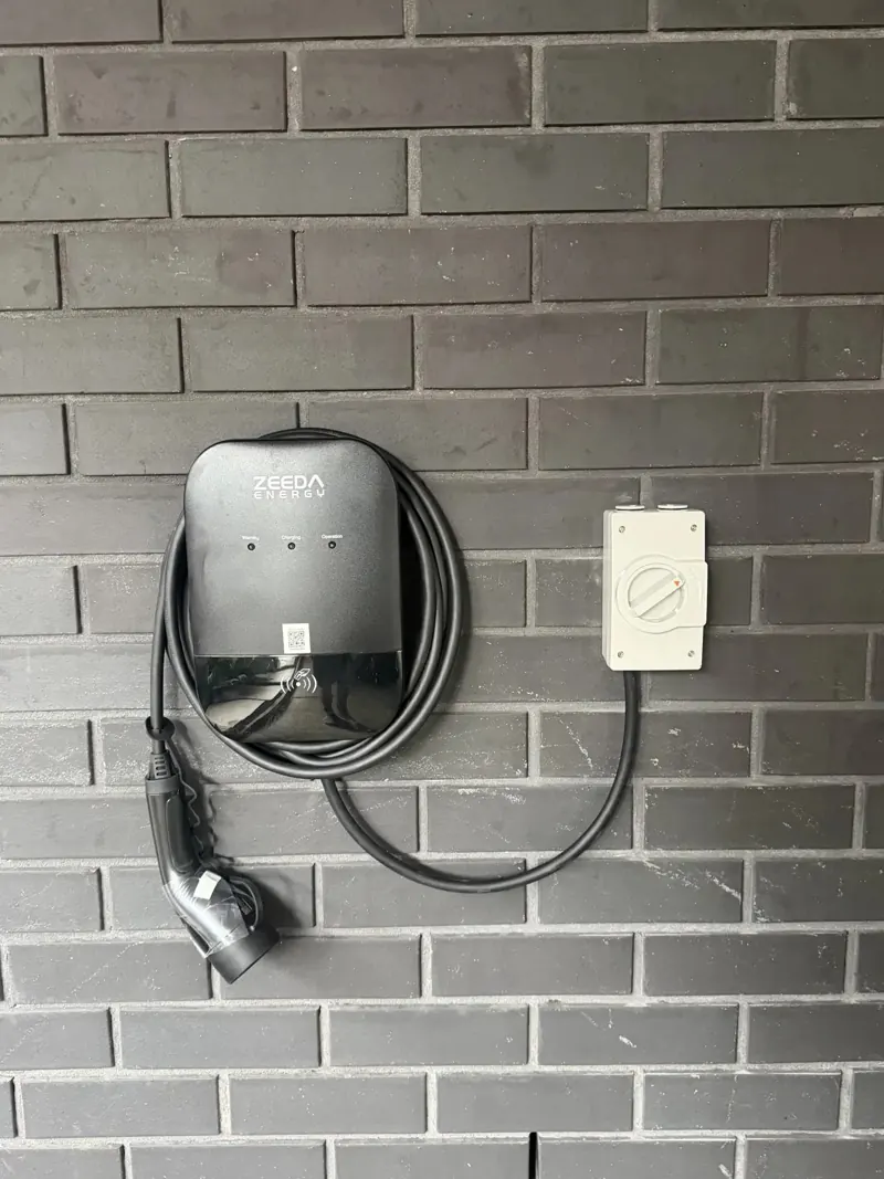Wall mounted EV charger and isolator installed on a brick home by Pender Electrical